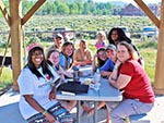 A small group sits at the picnic table under a pavilion in the Tent City camping area.