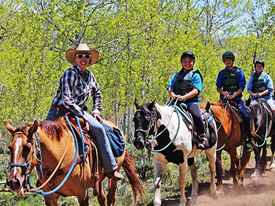 A wrangler and small group of riders smile from atop their horses.
