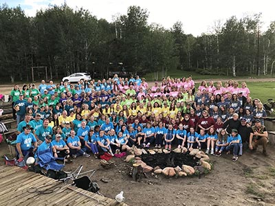 A large group of young women sit around the Red Creek Fire Pit as viewed from the Stage.