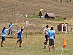 Several people engage in a game of Frisbee Golf; one Frisbee can be seen in the air.