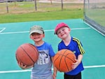 Two young boys hold basketballs. They like the game their fathers play.
